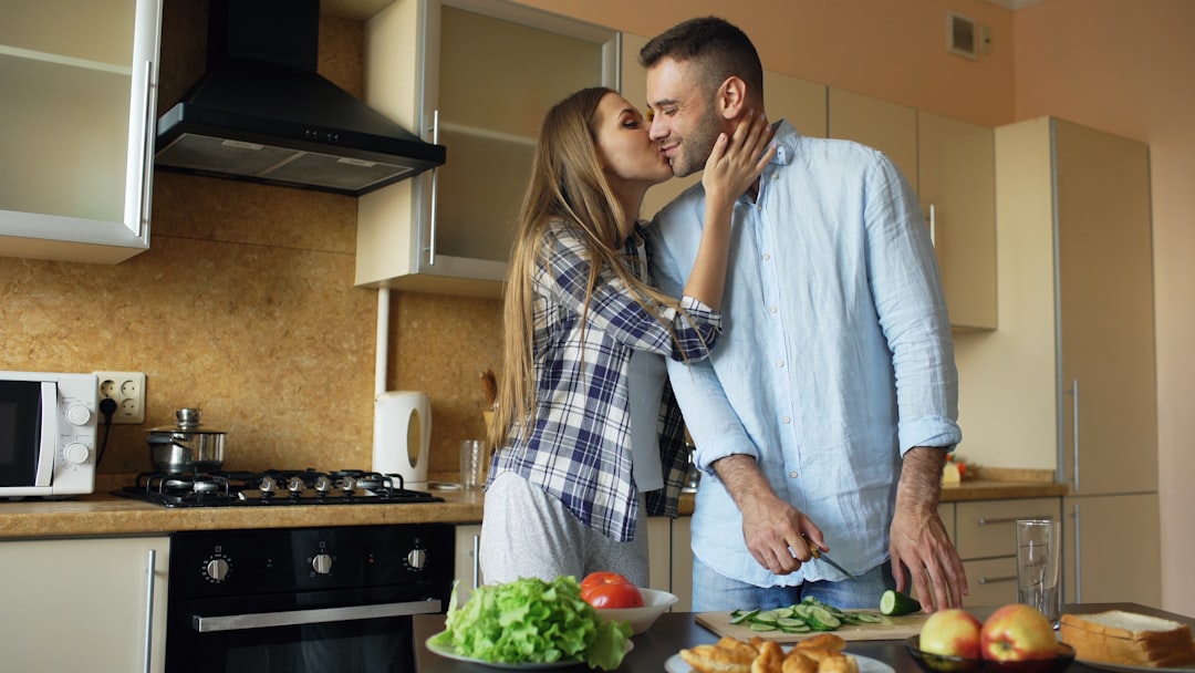 Couple kissing in a modern kitchen while preparing food.